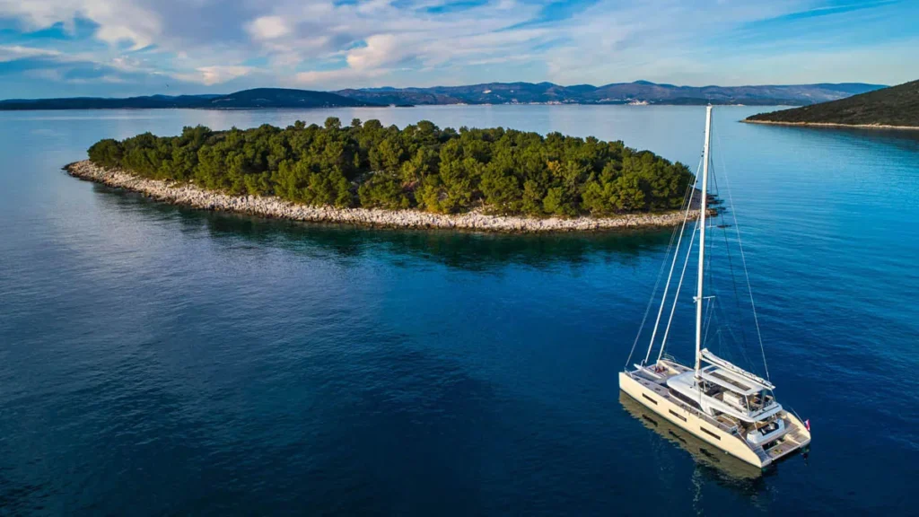 Catamaran Sailing Near a Pine covered Island in Calm Blue Waters with Distant Hills on the Horizon