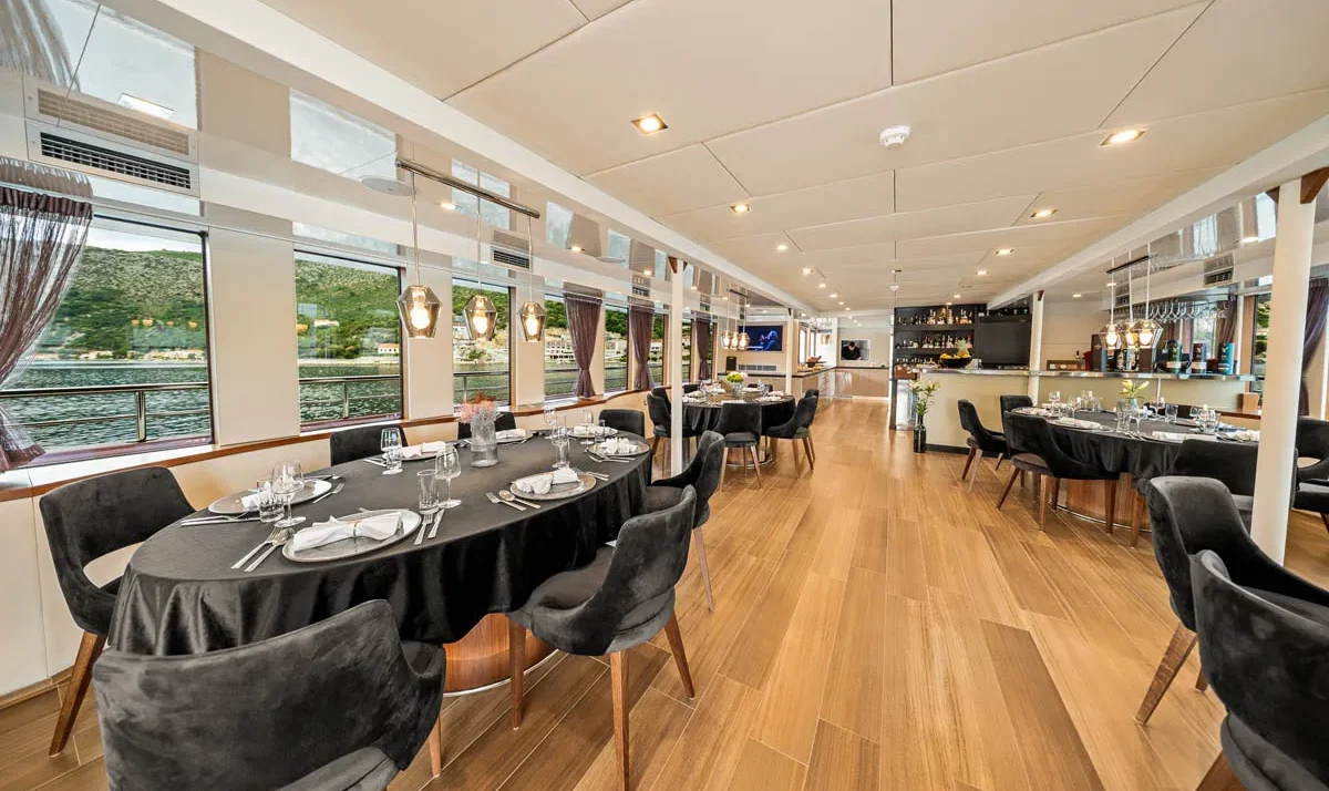 Elegant dining room on a boat Yolo with black-tableclothed tables, pendant lights, and a water view through large windows.
