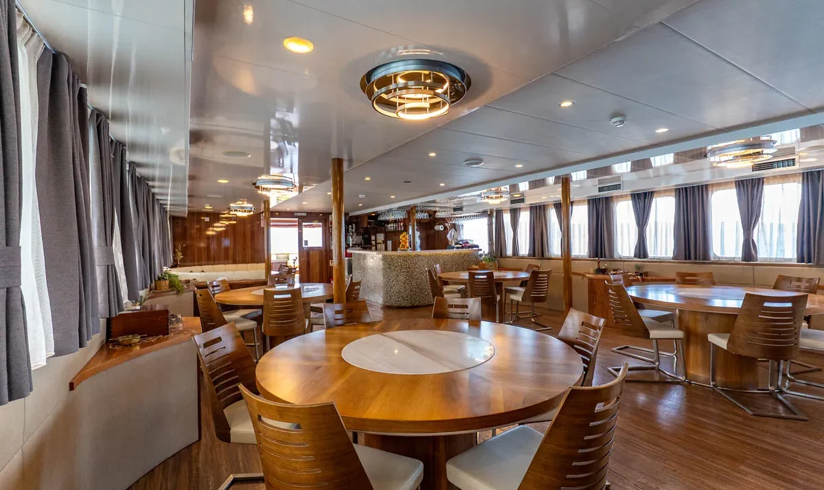 Elegant IL Mare yacht dining area with round wooden tables, chairs, and large windows with curtains.