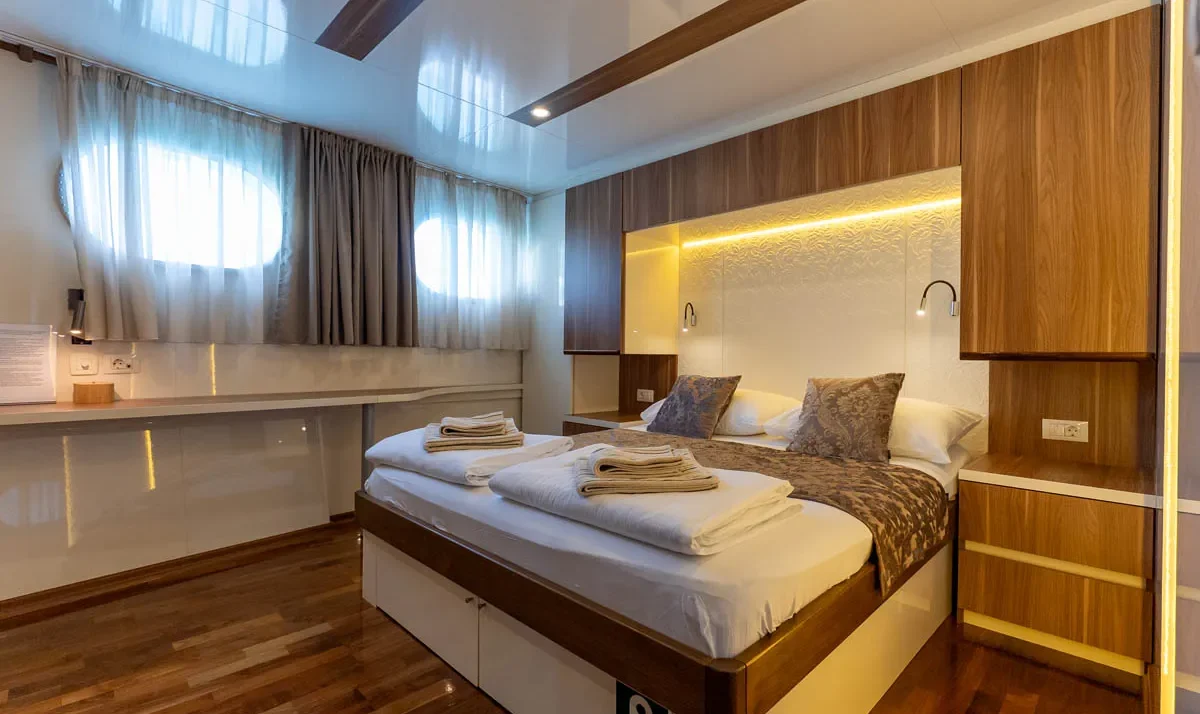 Modern hotel-style bedroom with a large bed, wood paneling, and built-in storage; warm backlit headboard creates a cozy glow.