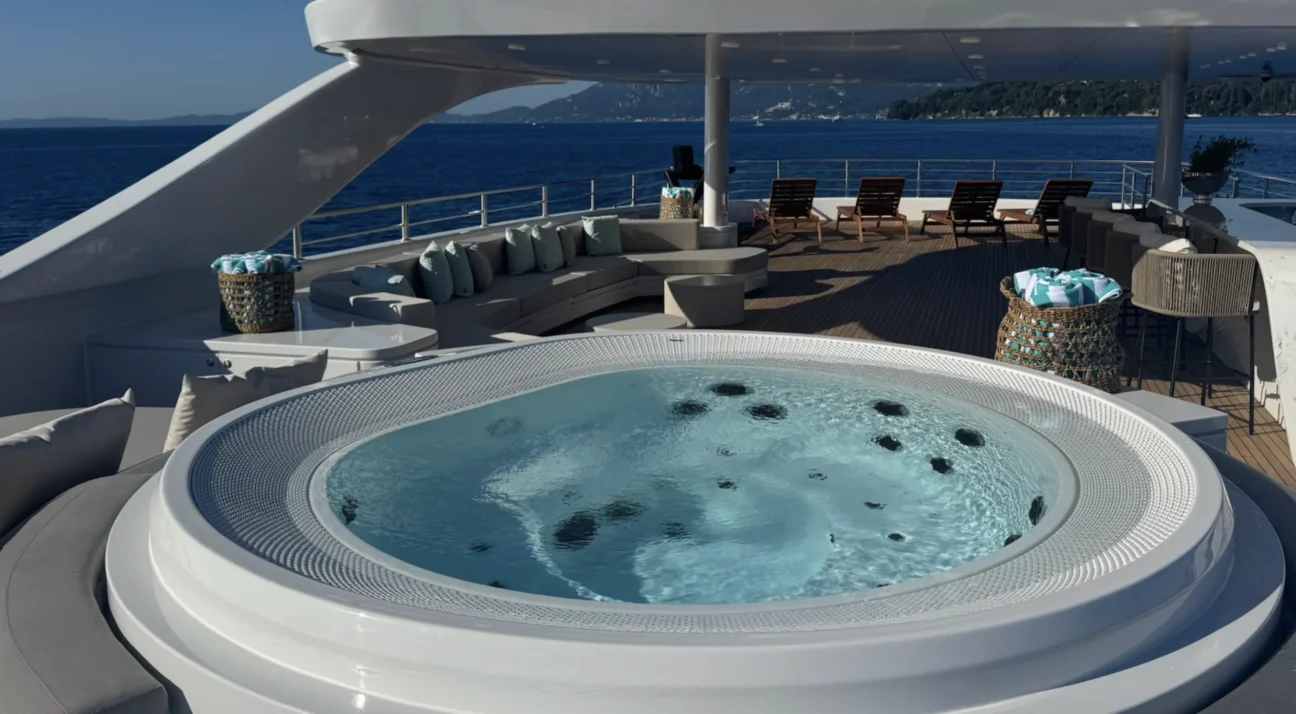 Luxurious yacht deck with a round hot tub in the foreground, beige seating, and ocean view on the horizon.